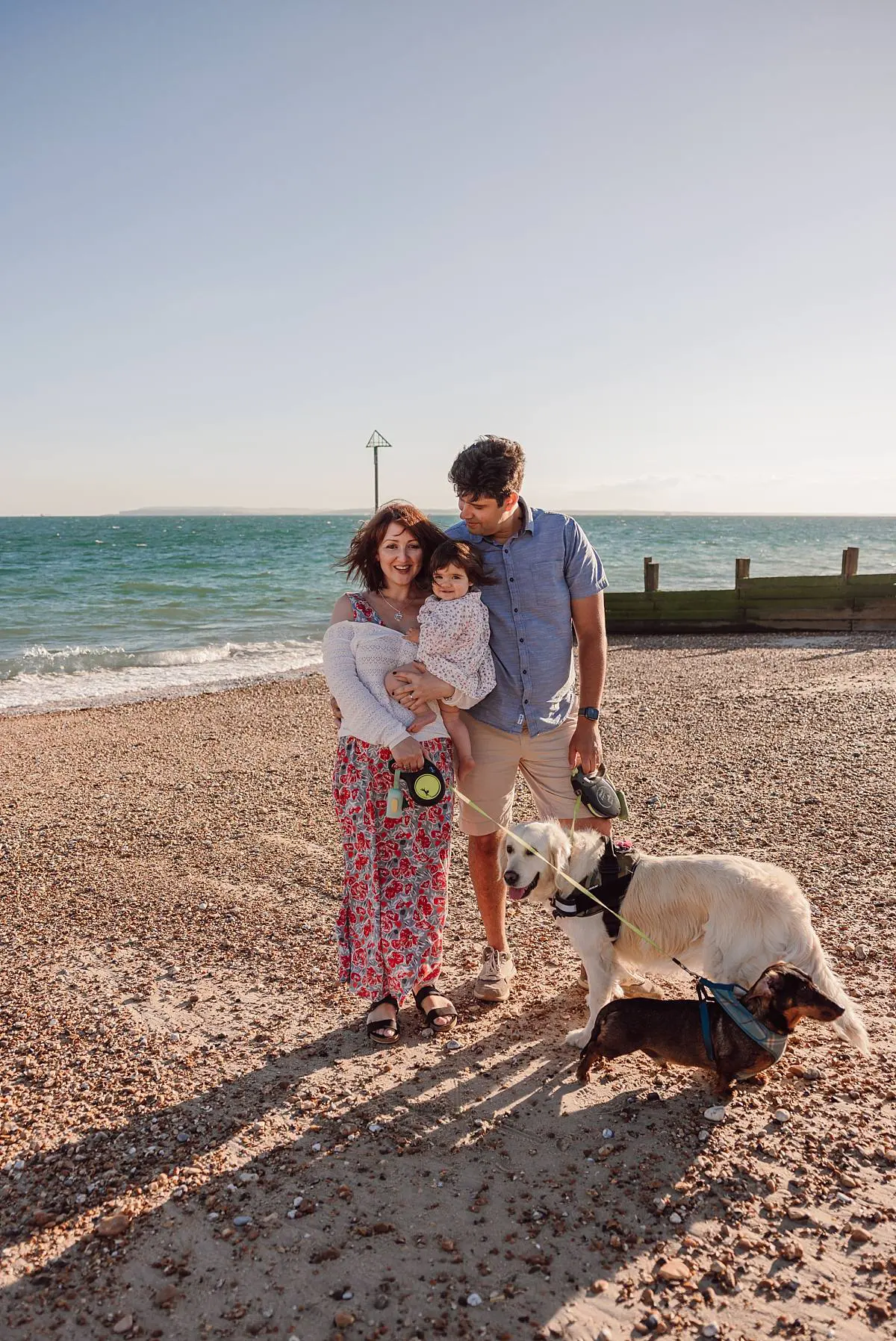 Family enjoying a sunset beach photo shoot on Hayling Island with their two dogs and one-year-old daughter