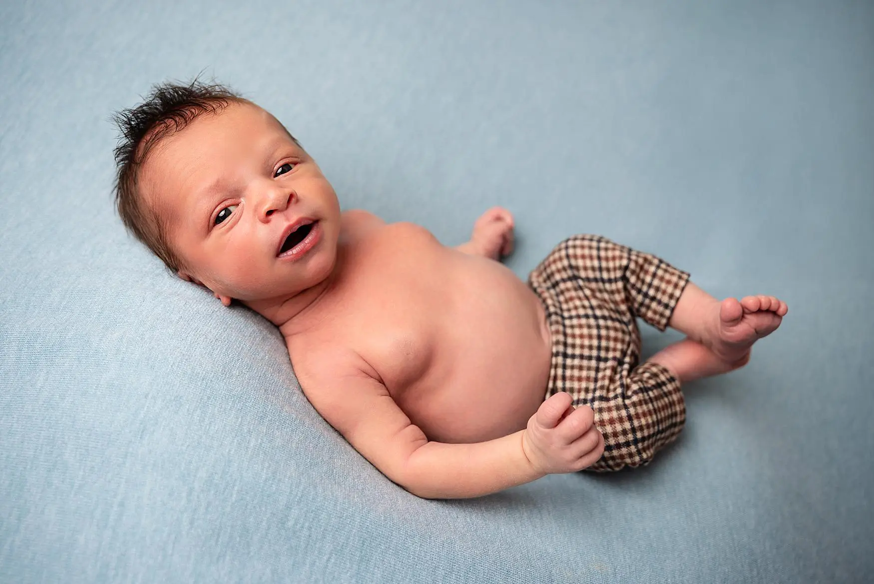 Newborn baby lying on a soft blue blanket, looking alert in patterned trousers newborn photography Waterlooville