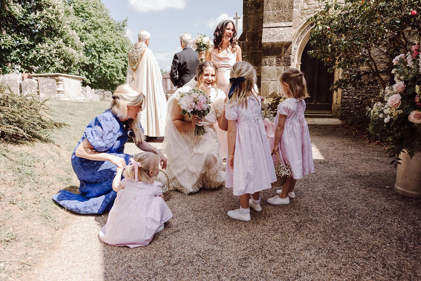Bride greeting flower girls outside the church in Harting near Petersfield, photographed during a relaxed spring wedding in West Sussex.