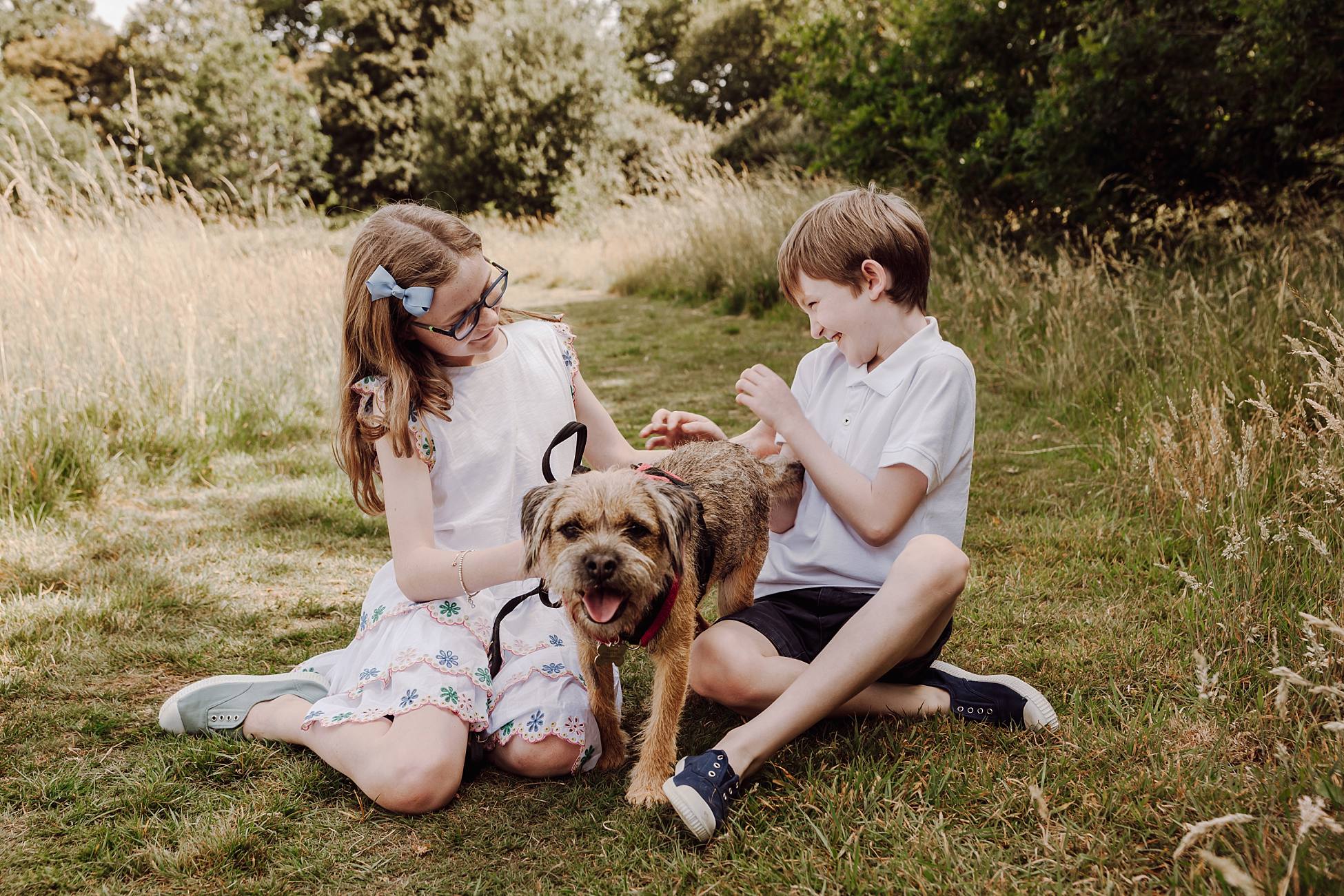 Brother and sister sitting in grass with their dog during outdoor family portraits