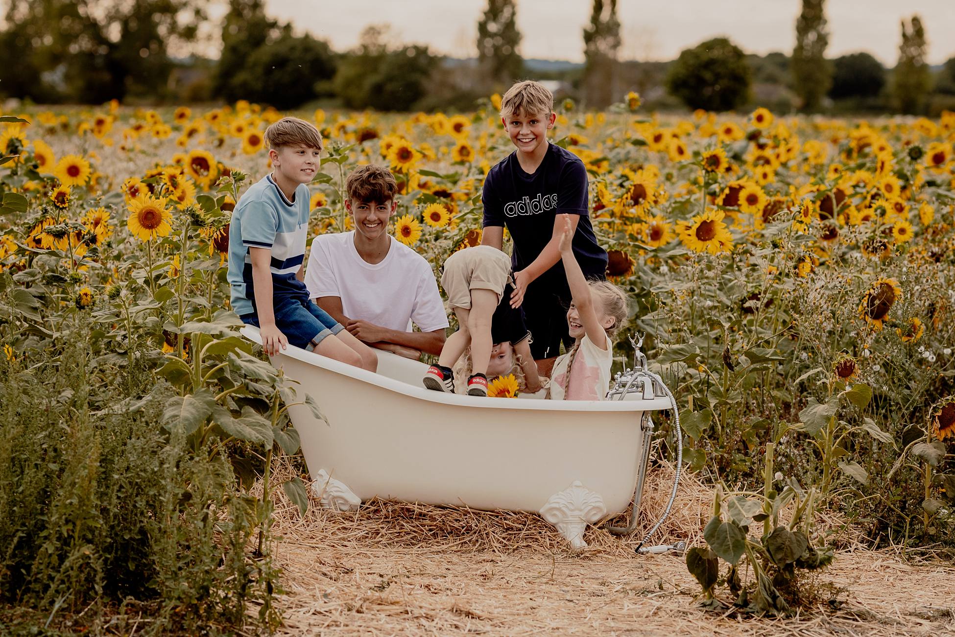 Children posing in white vintage bathtub surrounded by sunflowers in Hayling Island field