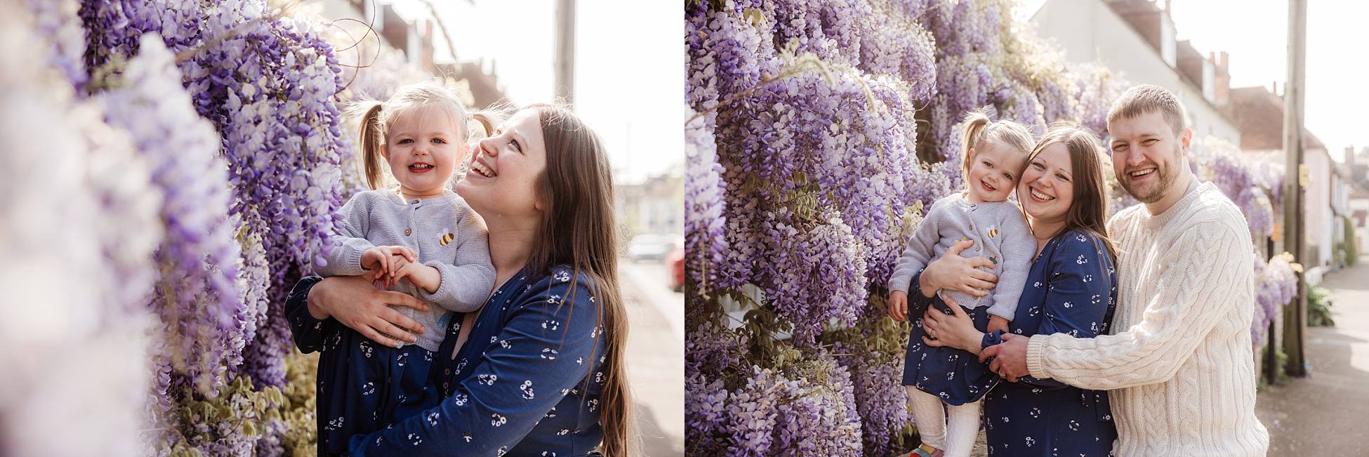 Parents cuddling toddler under wisteria flowers in Portchester