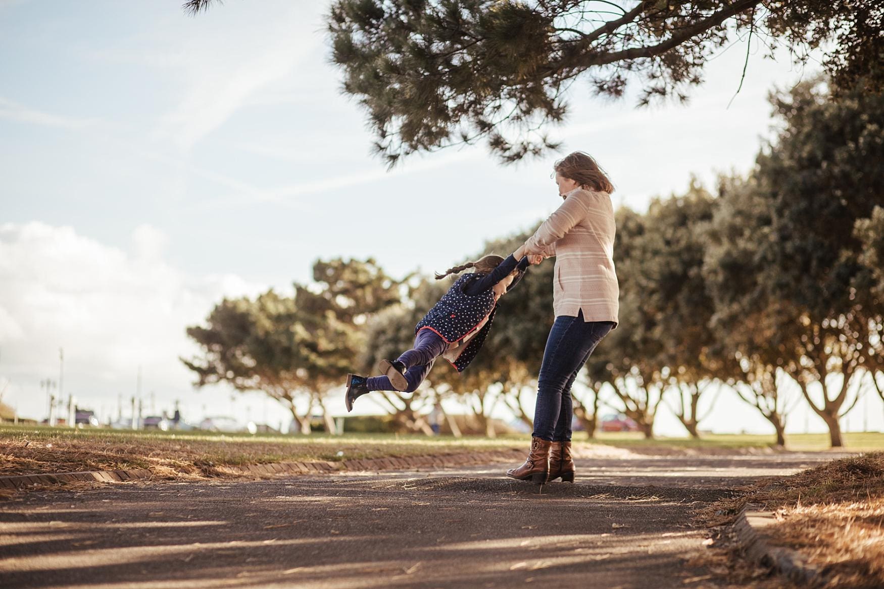 Mother spinning her daughter playfully under the trees at Southsea, Portsmouth