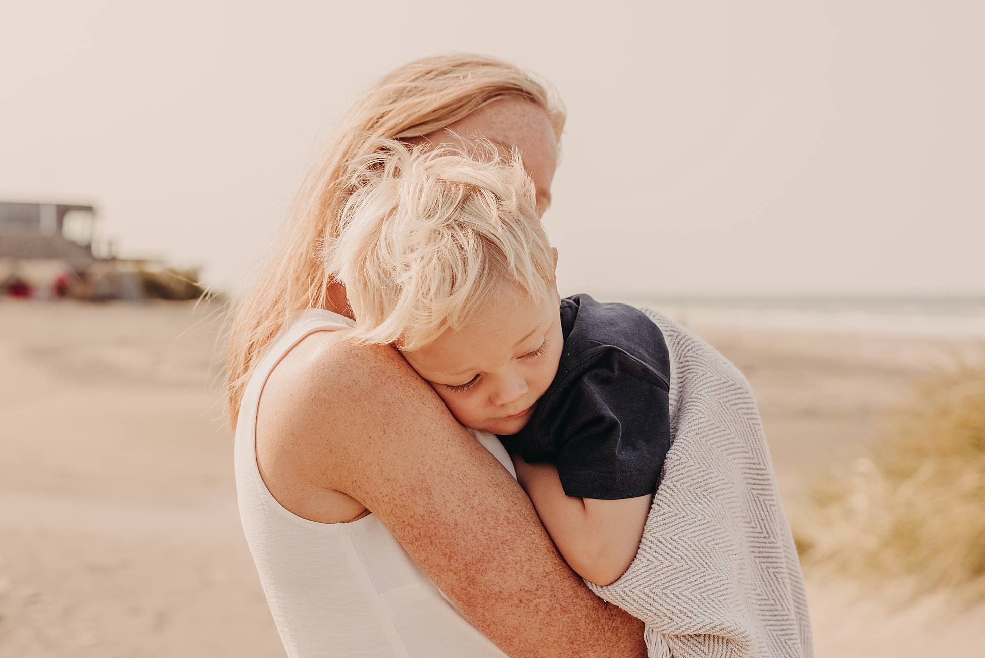 Mother cuddling her young son near a beach hut at West Wittering Beach