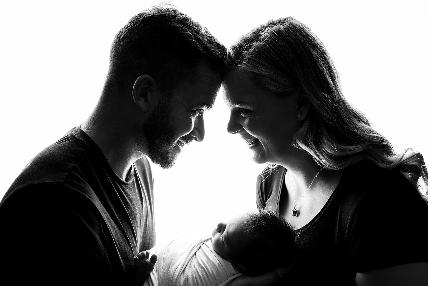 Silhouette portrait of parents smiling at each other while holding their newborn baby