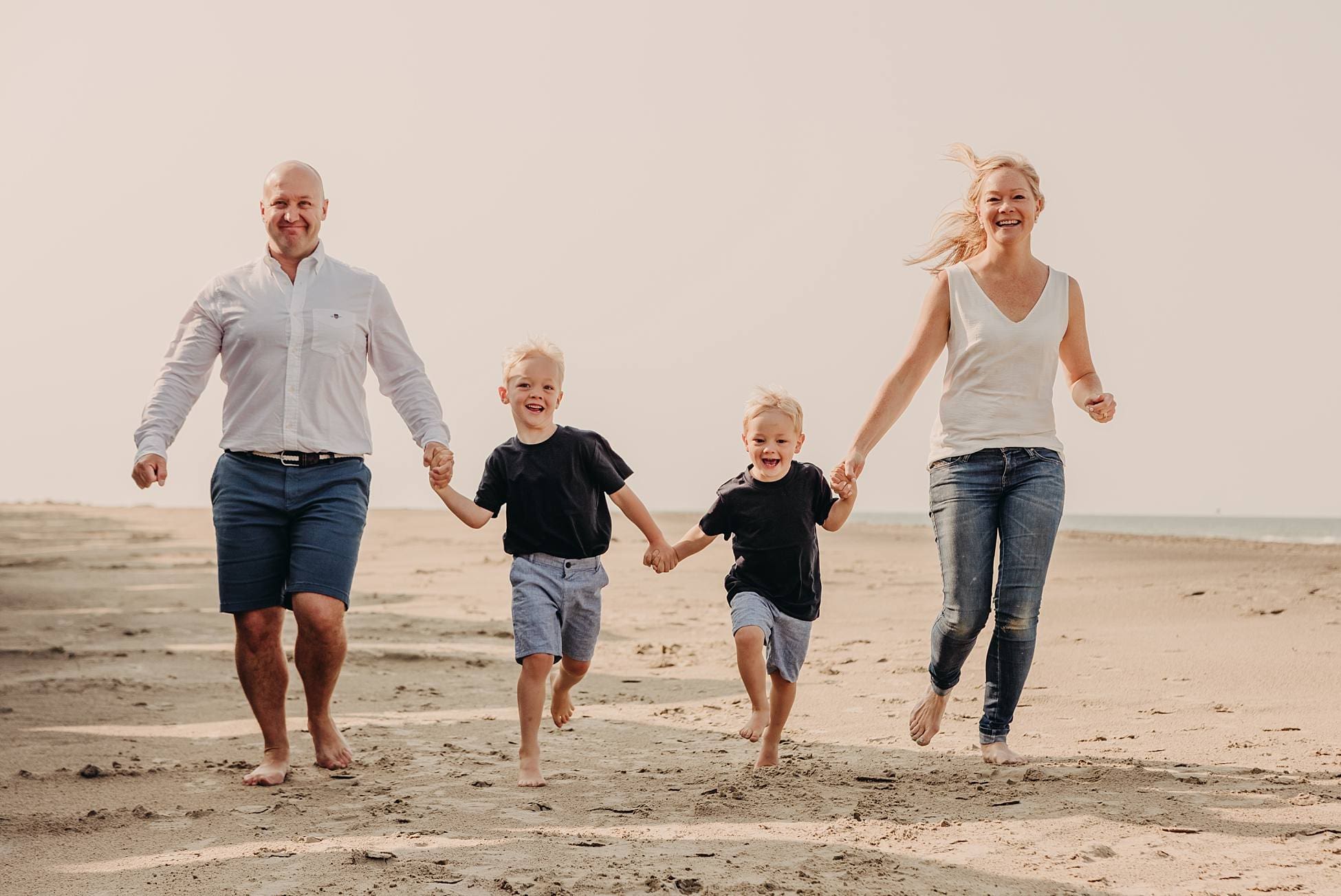 Family running across the sandy beach during their West Wittering summer photography session