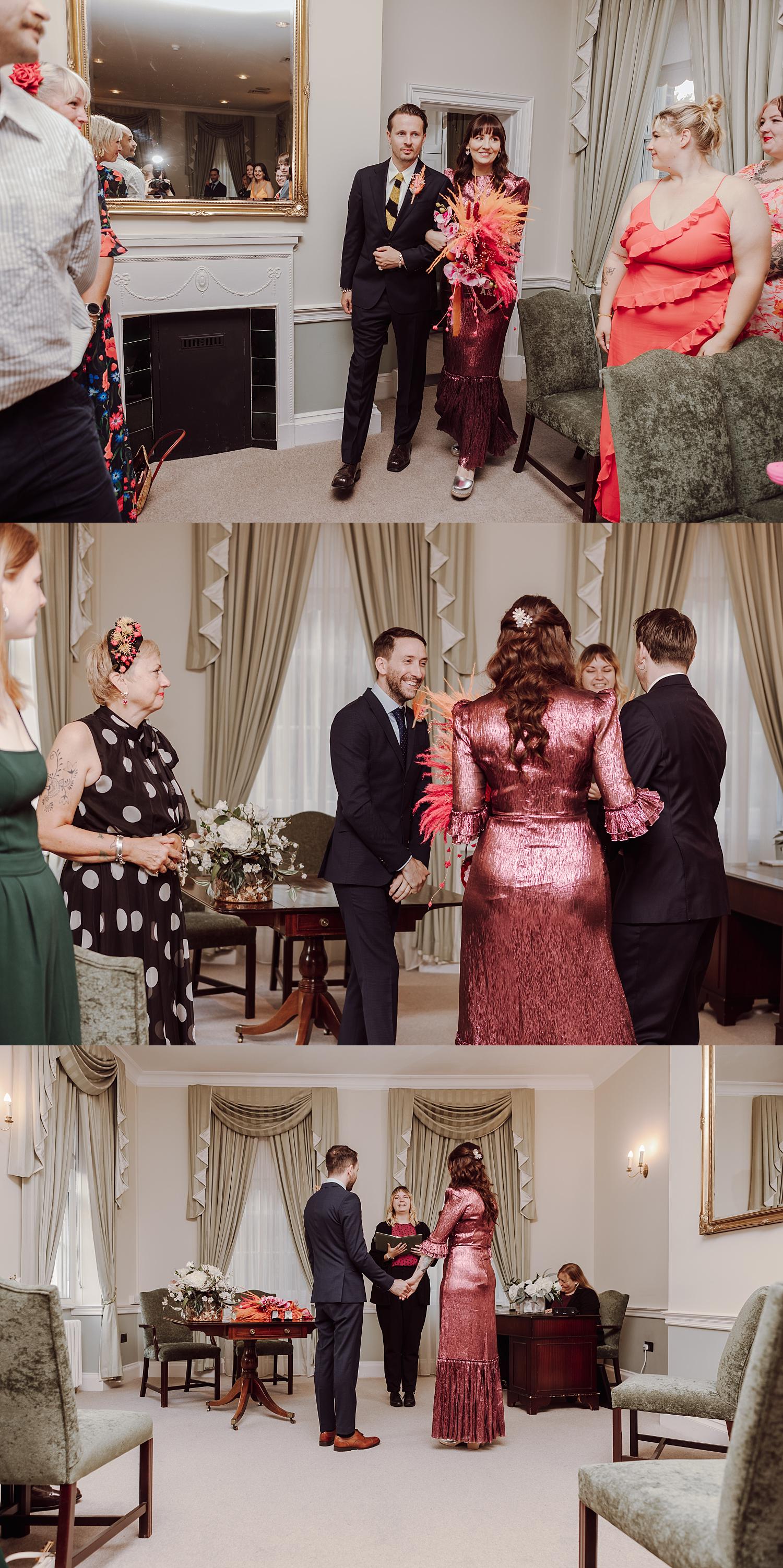 Bride entering the ceremony room during a Portsmouth Register Office wedding wearing a deep rose metallic dress and holding a vibrant bouquet