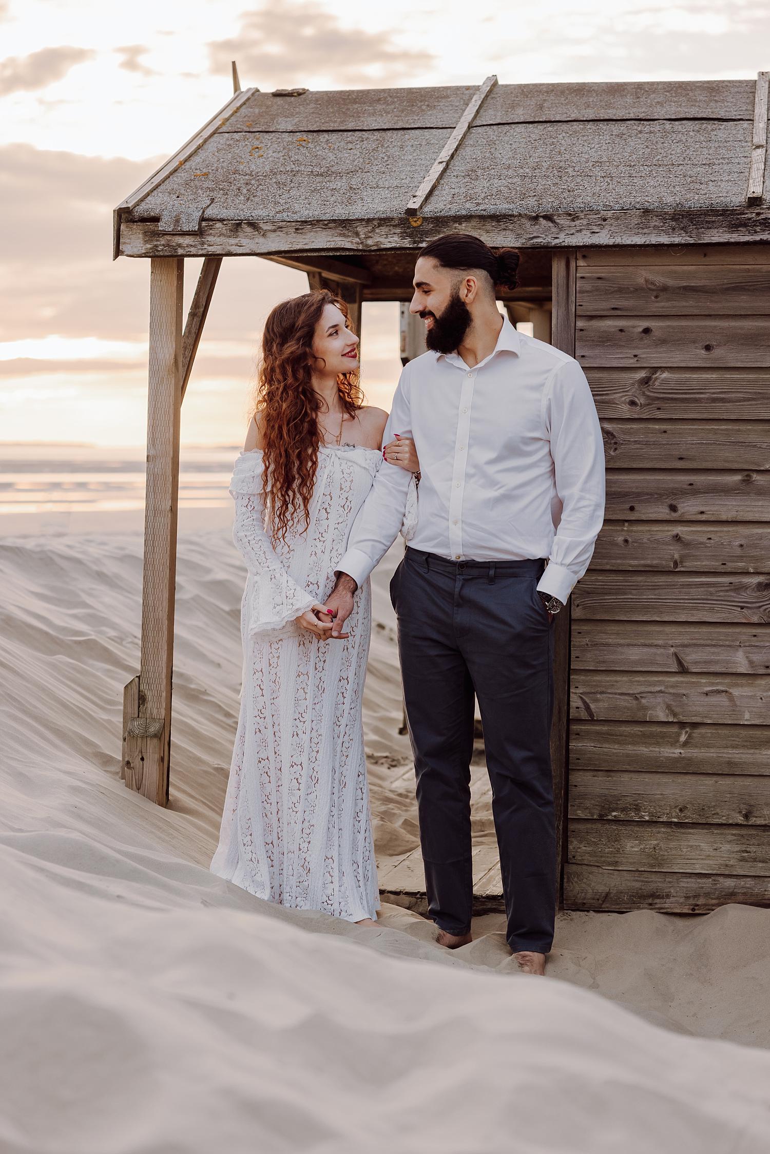 Romantic engagement photo of couple walking through sand dunes at West Wittering Beach in West Sussex.