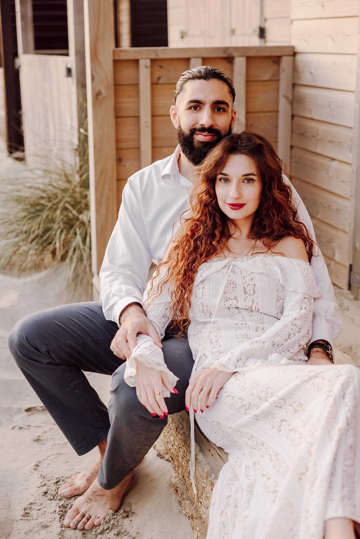 Golden hour engagement photography at West Wittering with couple seated on sandy dunes beside beach huts.