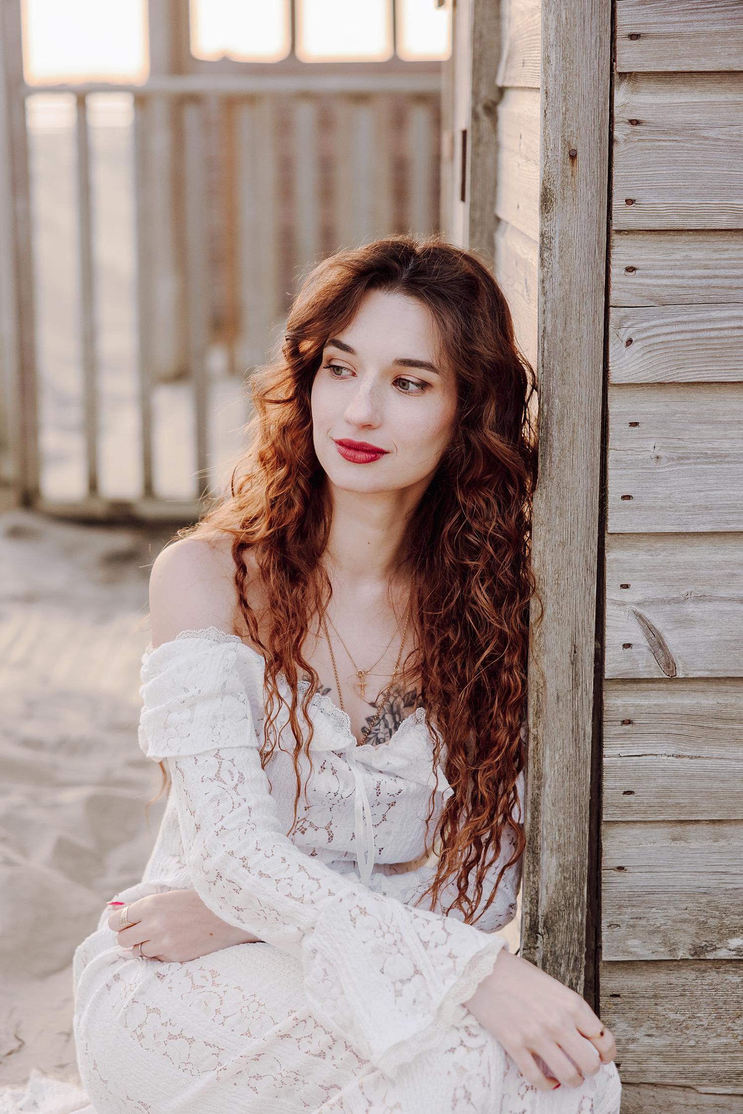 Romantic golden hour portrait of bride leaning against beach hut at West Wittering Beach in West Sussex.