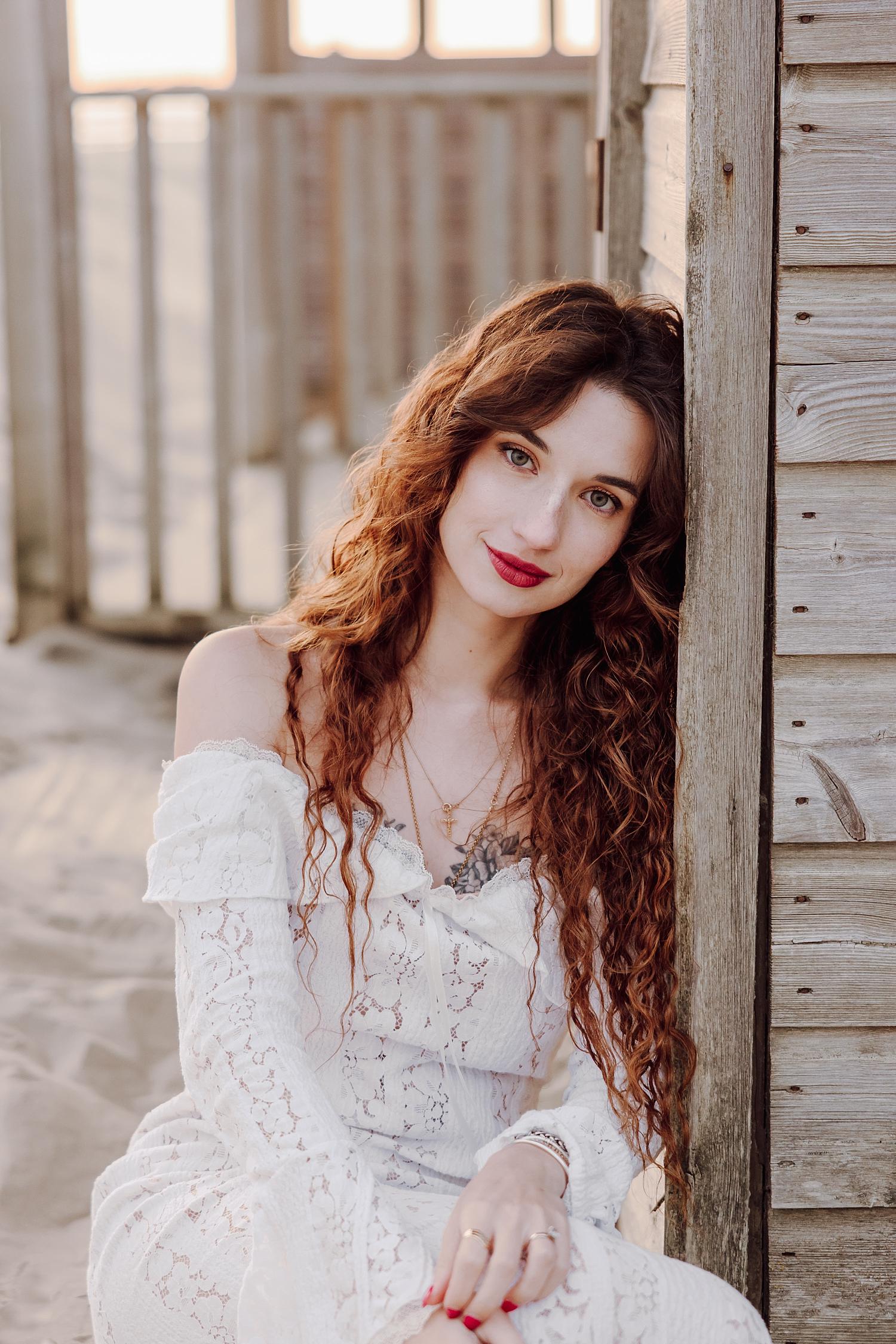 Close up portrait of bride to be with long red curls beside wooden beach hut at West Wittering engagement session.