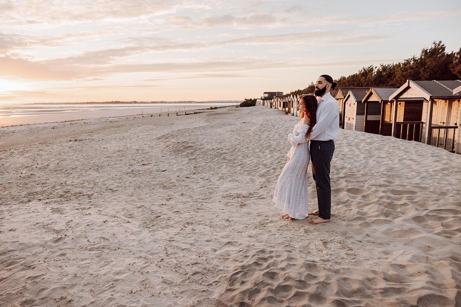Couple standing on West Wittering Beach at sunset with coastal huts and soft golden light in West Sussex