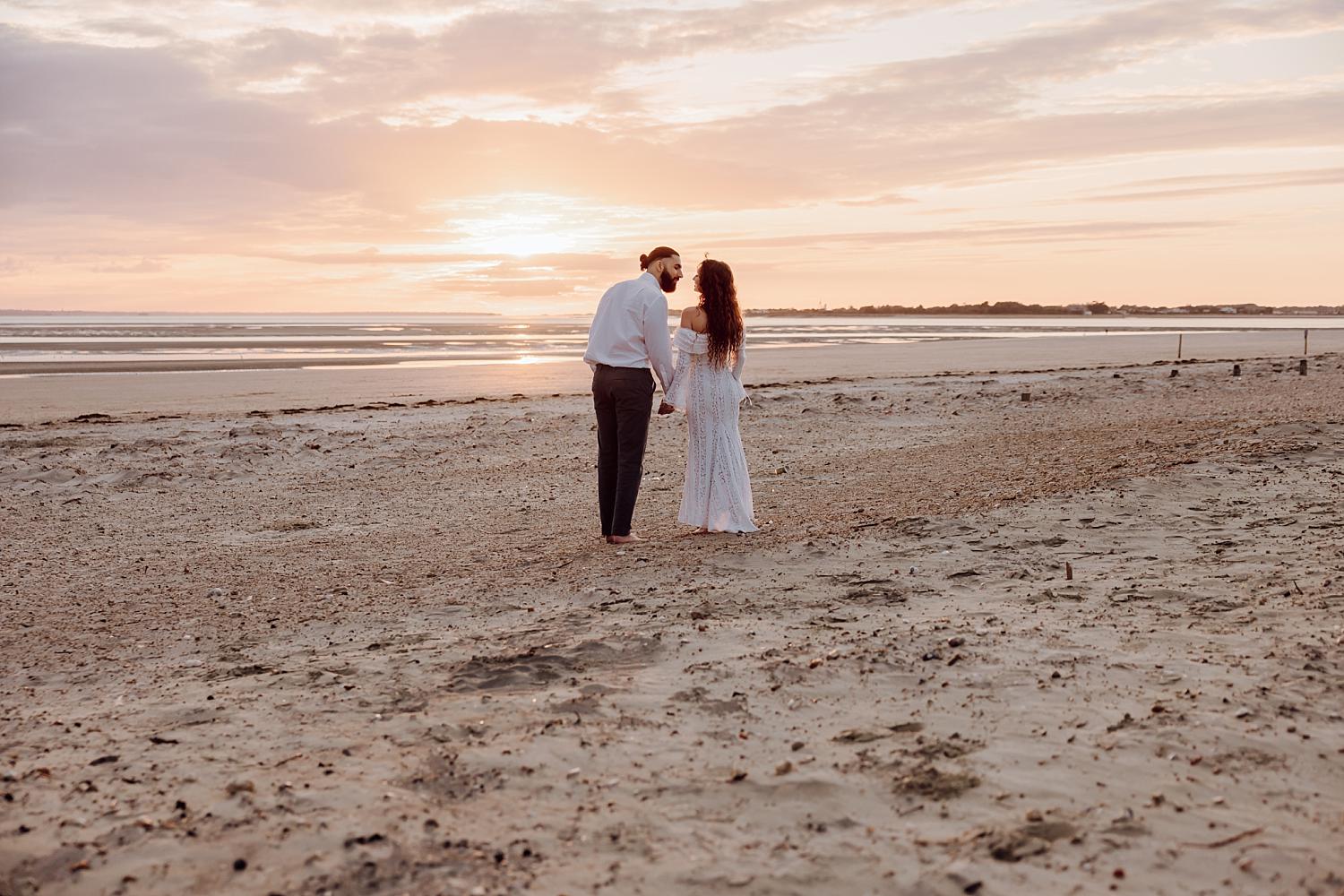 Romantic sunset engagement session at West Wittering with couple standing together overlooking the sea.