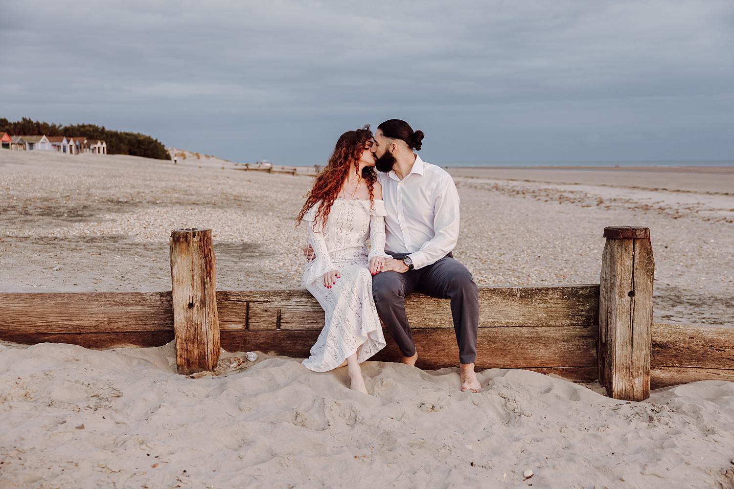 Intimate beach engagement portrait at West Wittering with couple sharing a kiss at sunset in West Sussex.