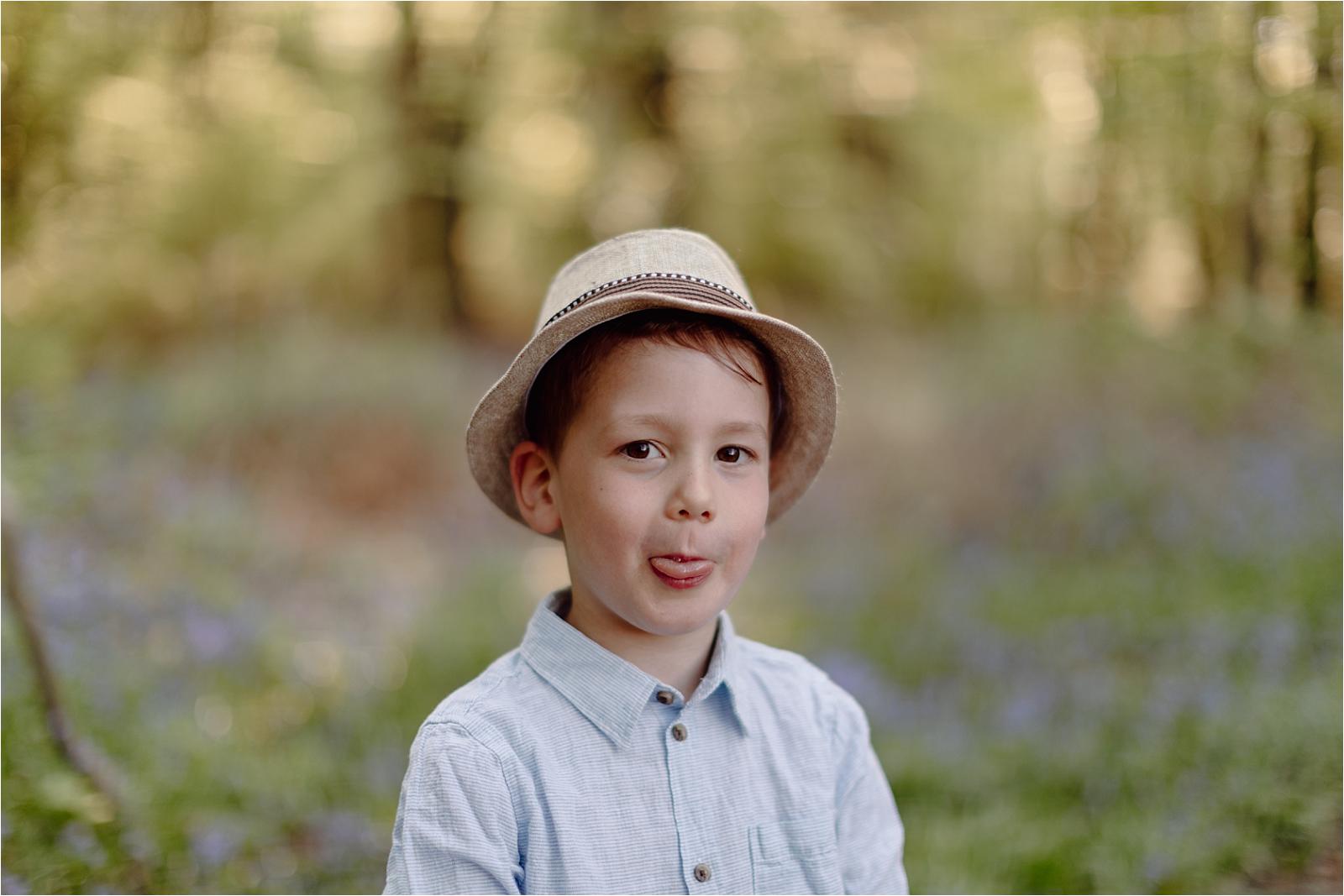 Young boy wearing hat in bluebell woodland in Hampshire, natural child portrait during spring mini session with soft light