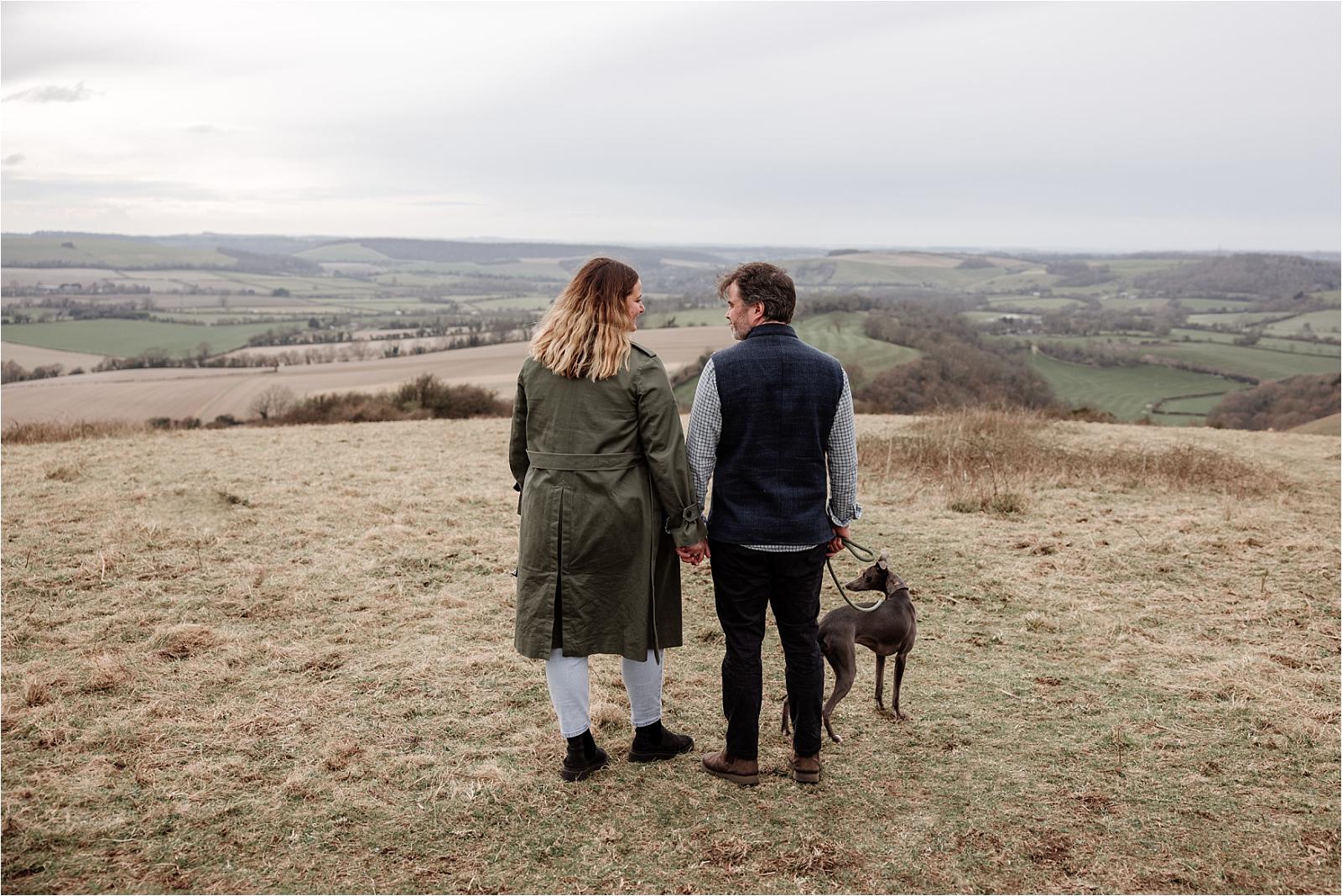 Couple walking hand in hand with their whippet across Butser Hill in autumn