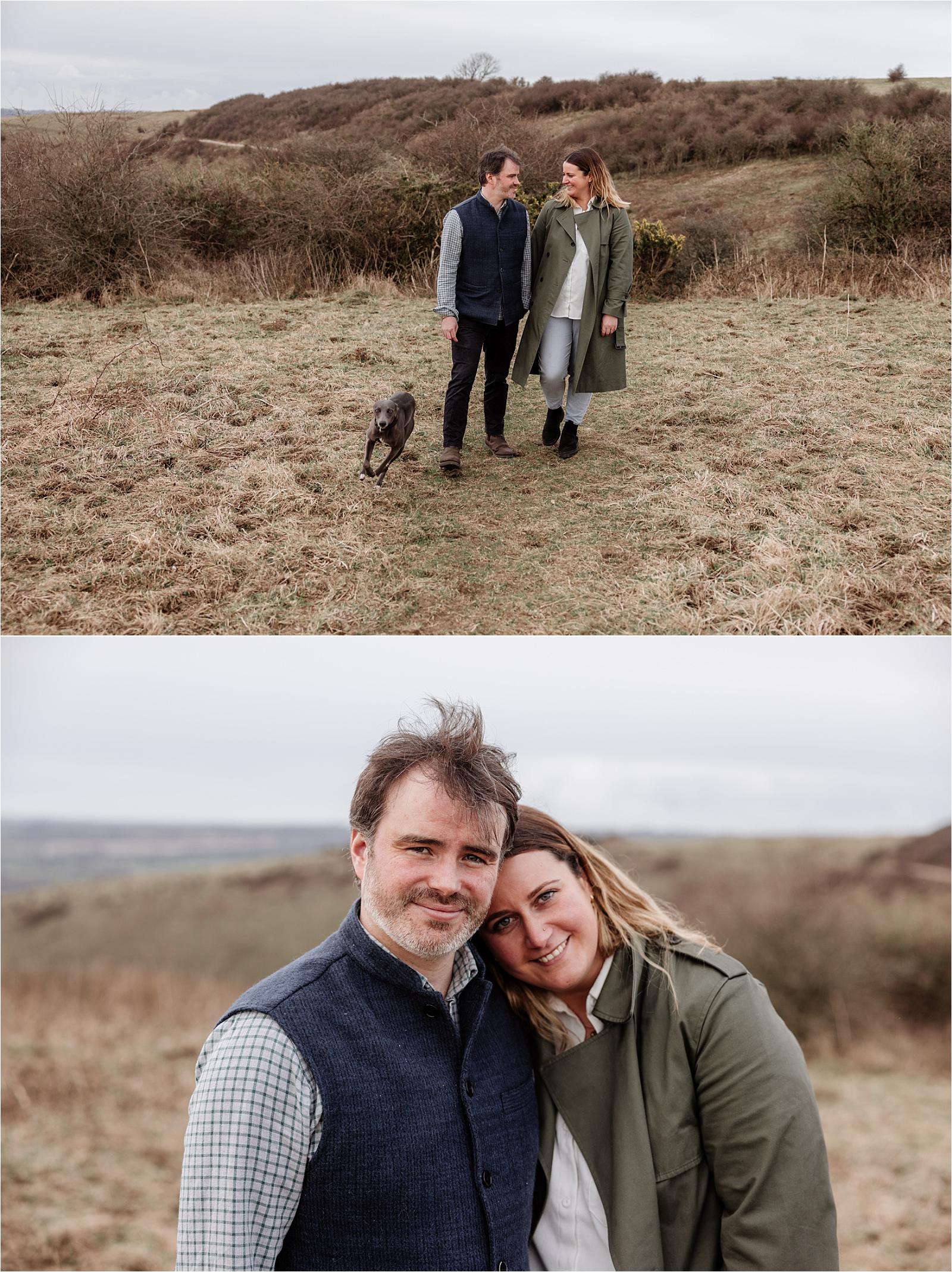 Couple walking through autumn heathland at Butser Hill with their whippet following behind