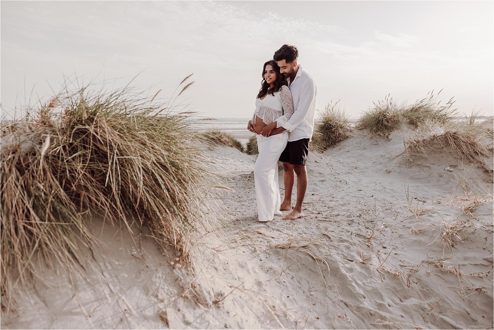 Expectant couple standing together among the dune grasses at West Wittering beach
