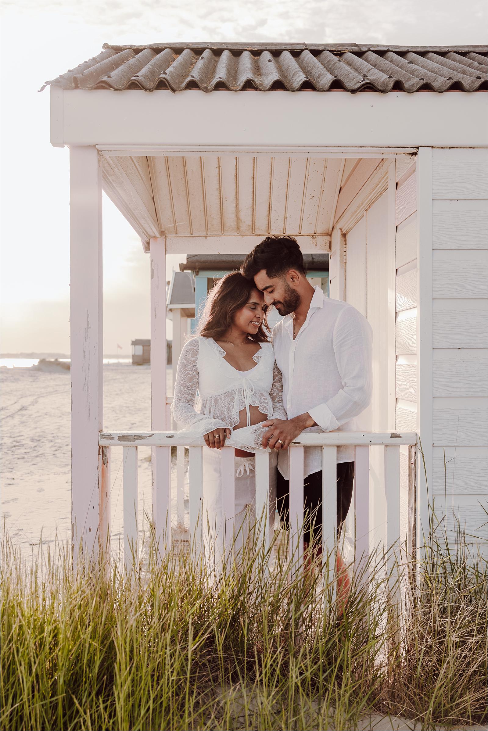 Mum-to-be and her husband sharing a quiet moment on a beach hut veranda during their West Wittering maternity session
