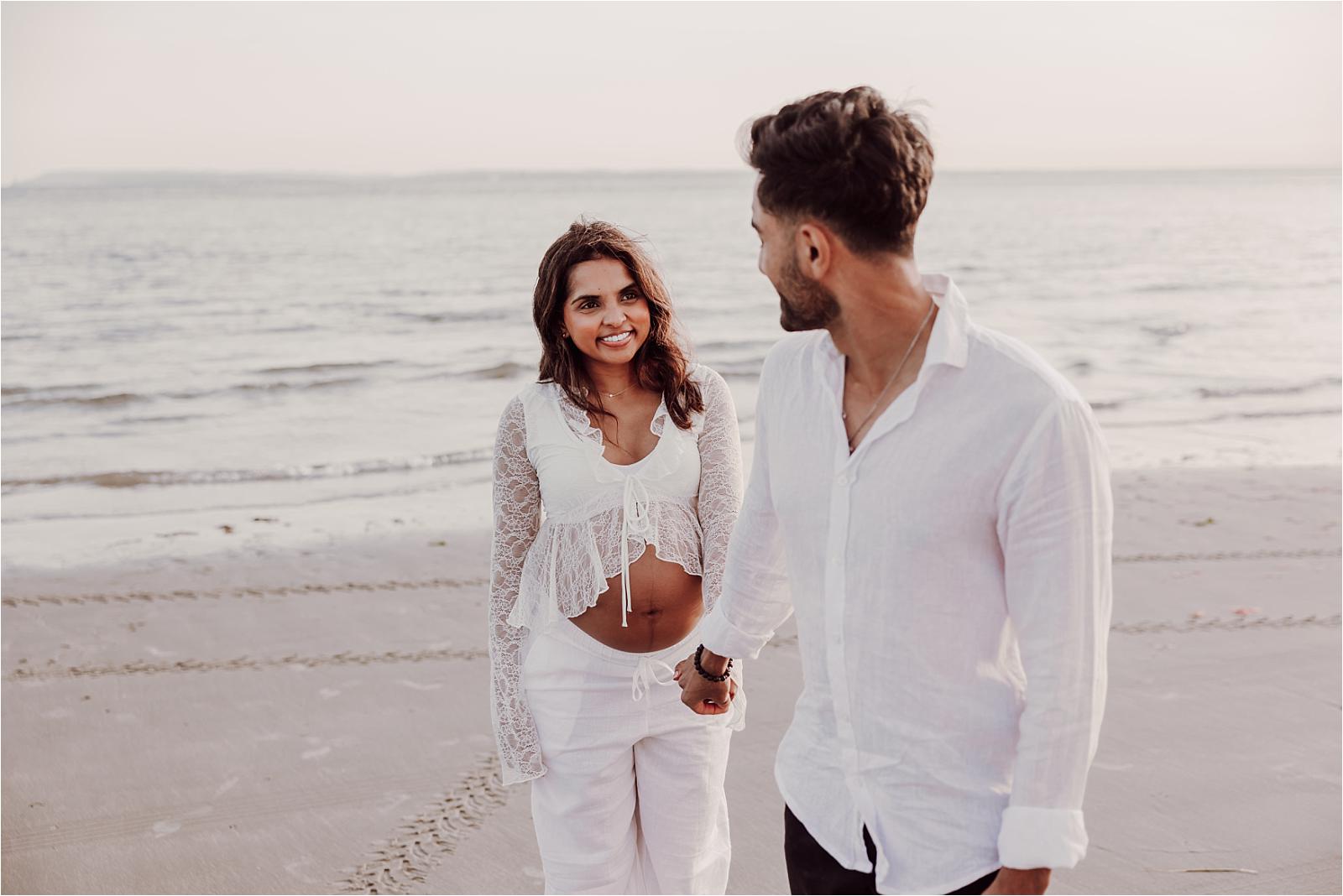 Expectant couple embracing by the shoreline during their West Wittering maternity session