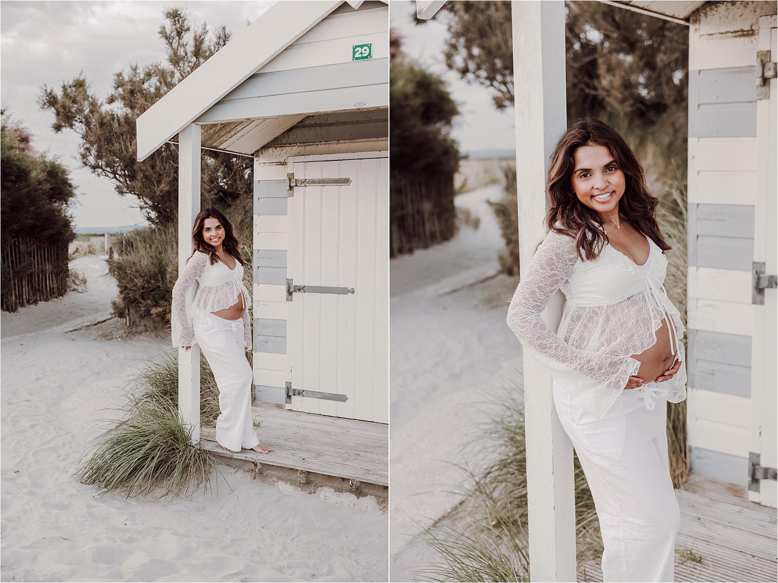 Expectant mother in white standing between colourful beach huts at West Wittering