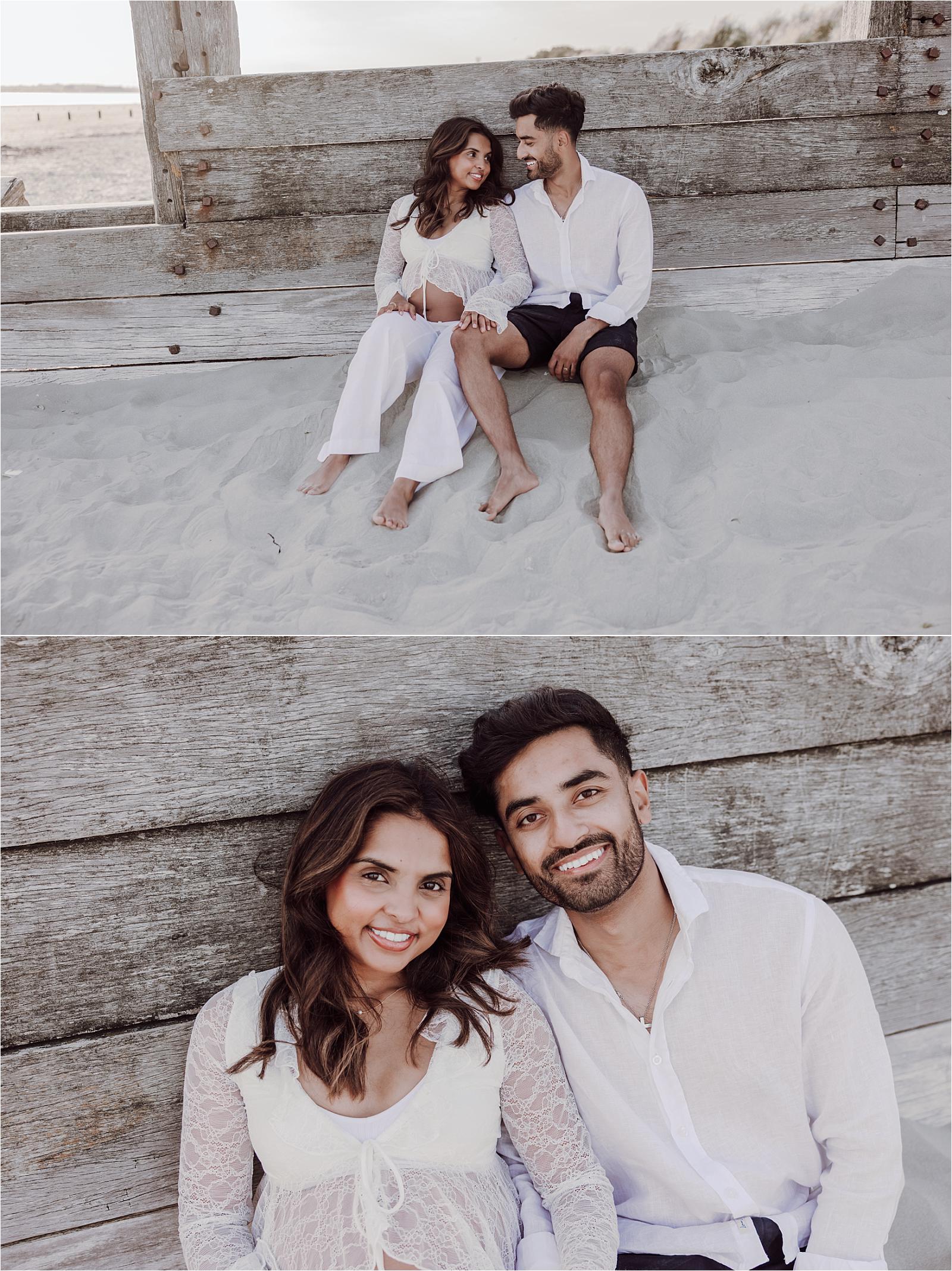 Couple sitting on the sand against wooden groynes at West Wittering at golden hour