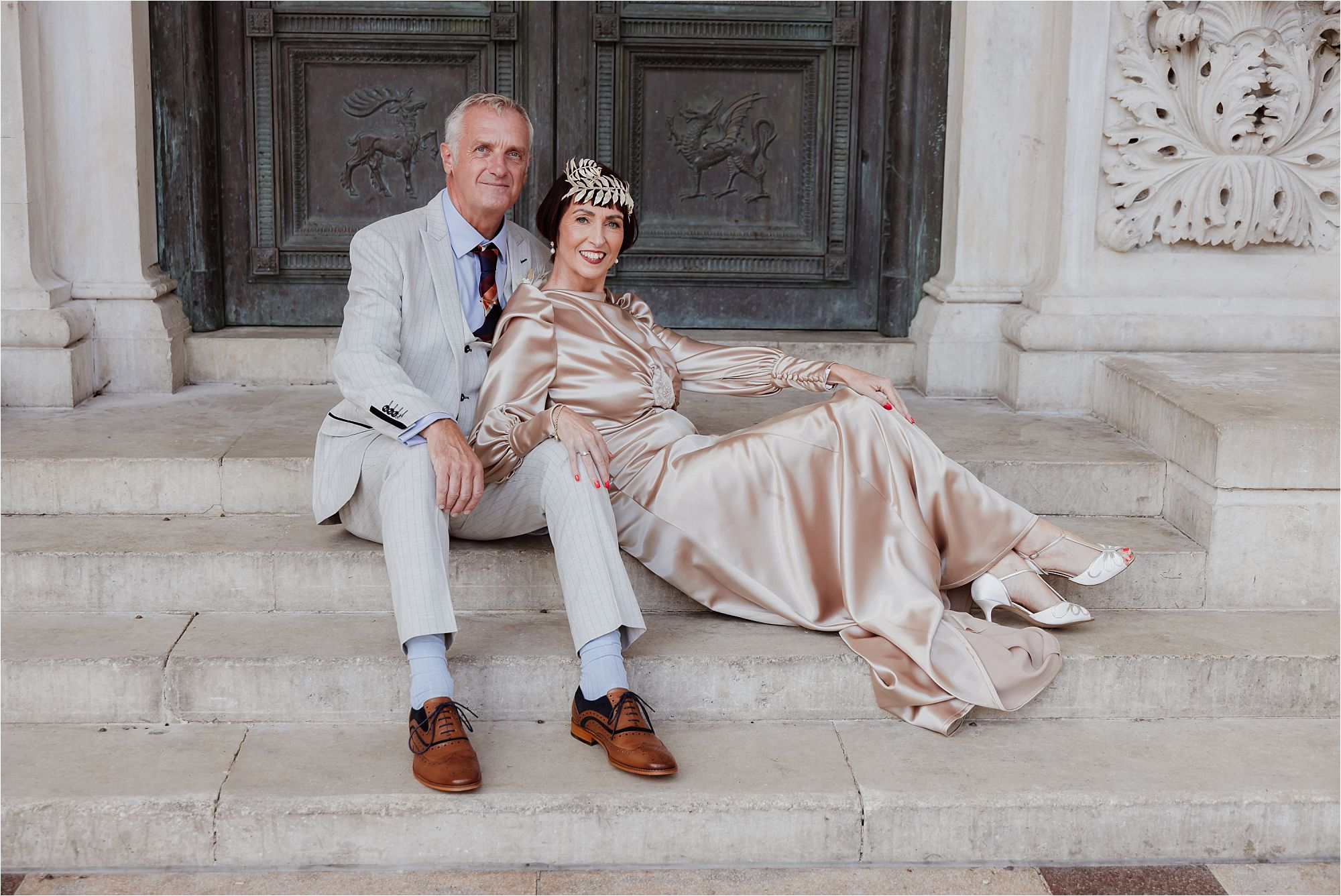 Groom seated beside the bride with her satin gown spread across the steps