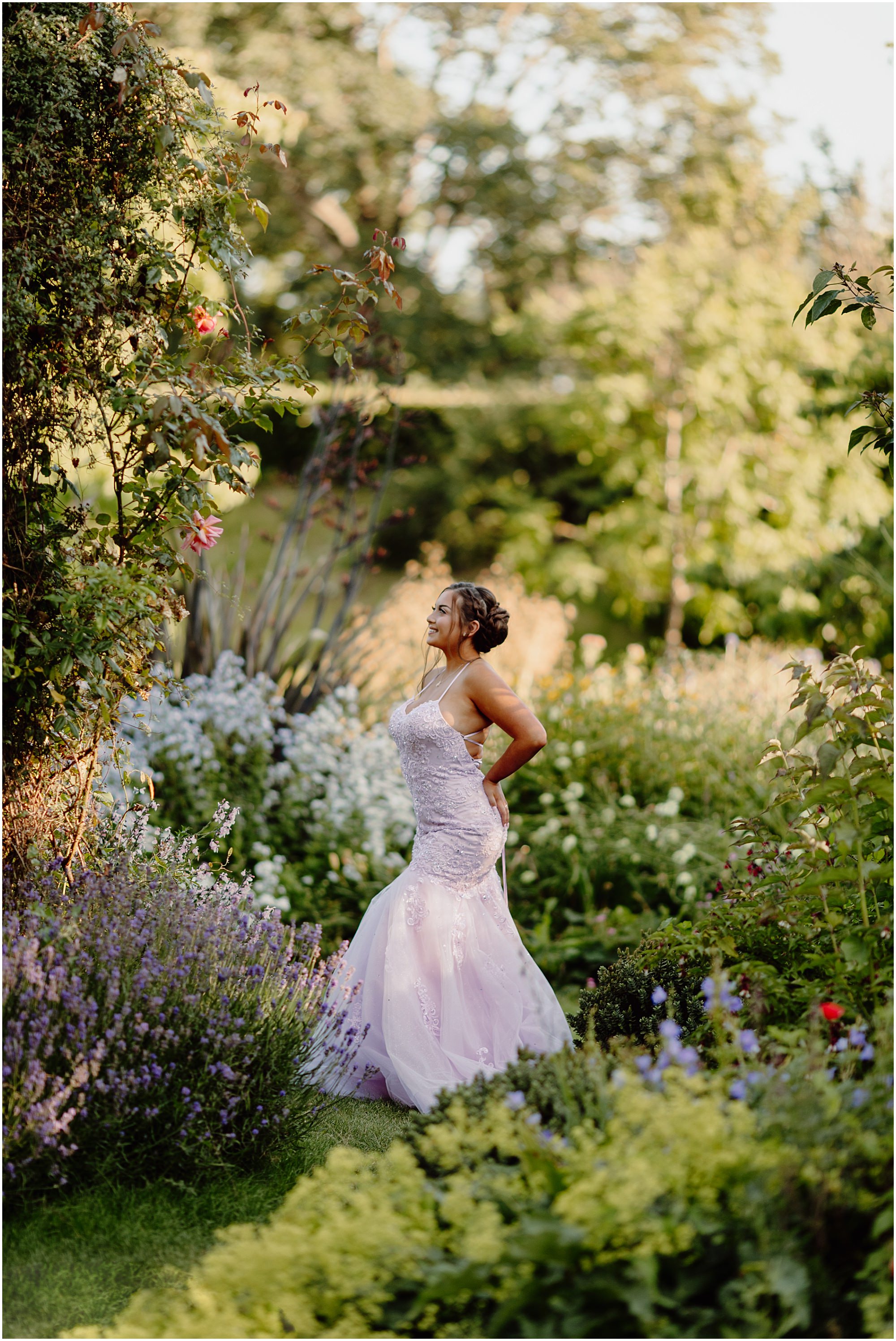 Walking away under the leafy arch: Teenager in a lilac prom dress walking beneath a flowering garden arch at golden hour