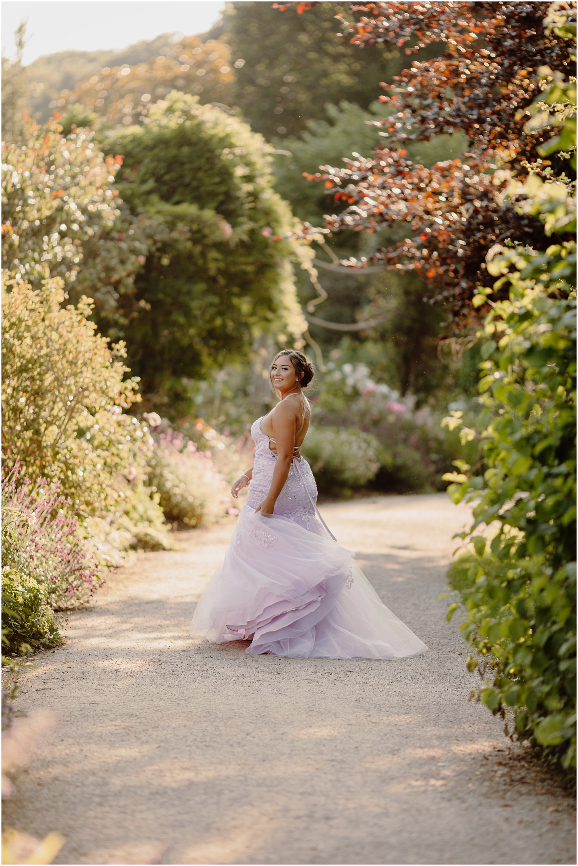 Single tall image, standing side-on among lavender and roses Prom photoshoot Chichester with a teenager standing among lavender borders at sunset