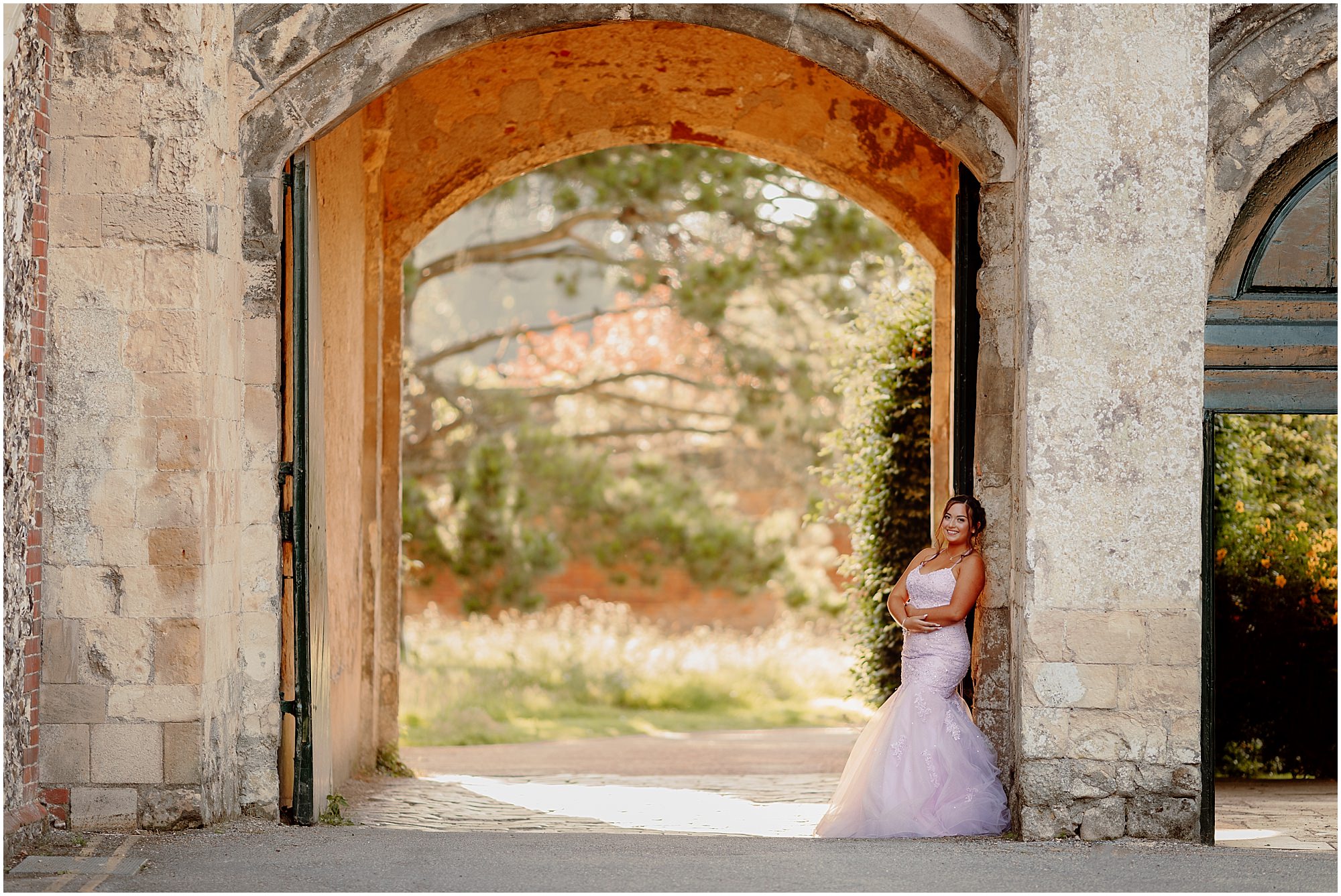 Standing in the stone archway looking out to the garden:
Teenager in a lilac prom dress framed by a stone archway in Chichester