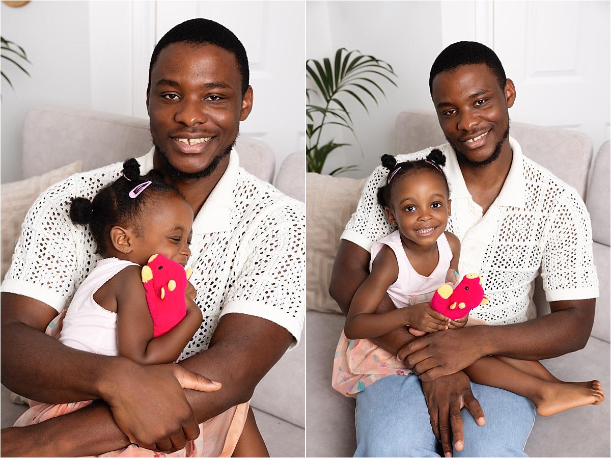 Dad holding his older daughter on his lap as she cuddles her favourite red toy