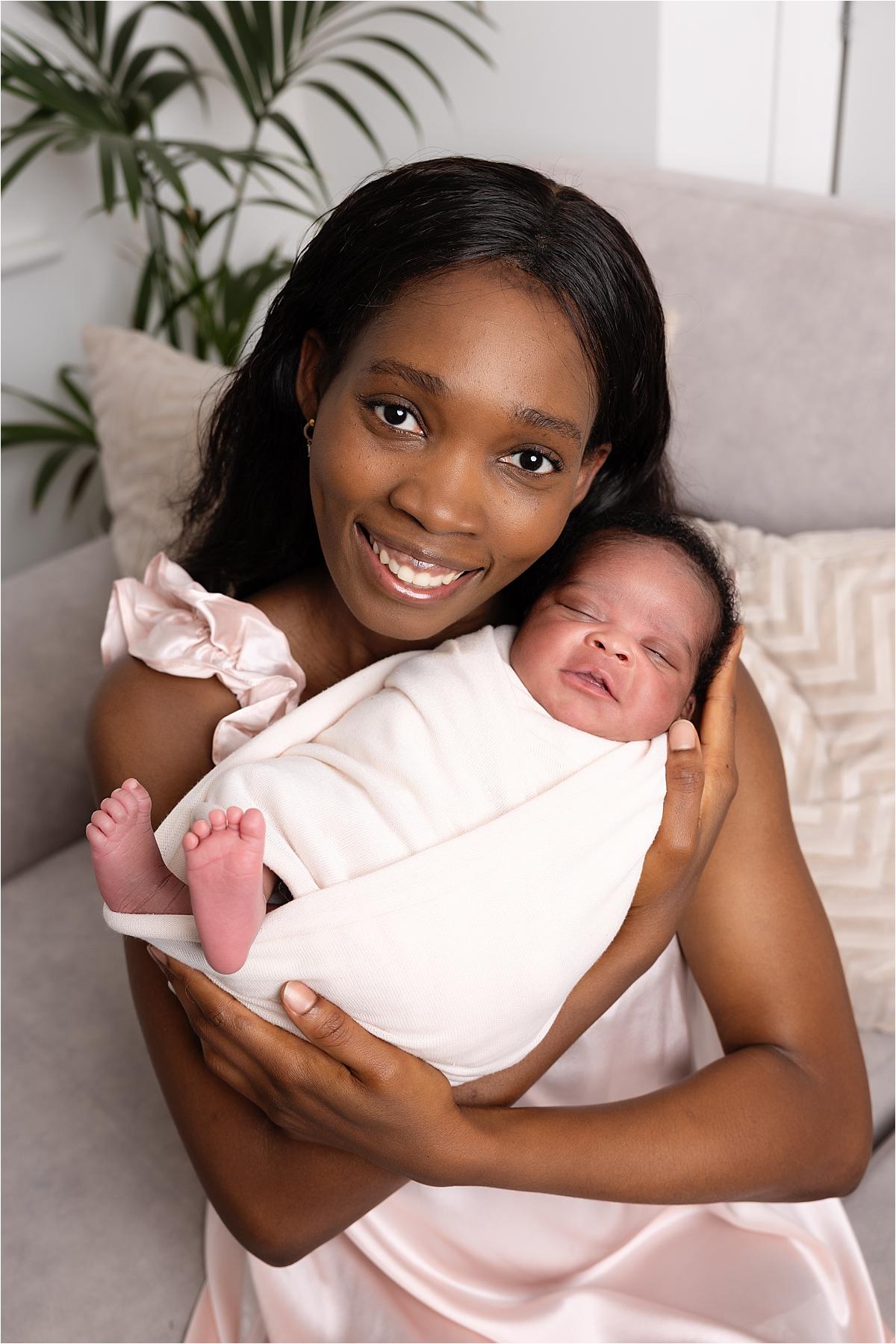 mum-holding-newborn-havant-at-home Mum smiling as she holds her newborn baby wrapped in cream on the sofa at home